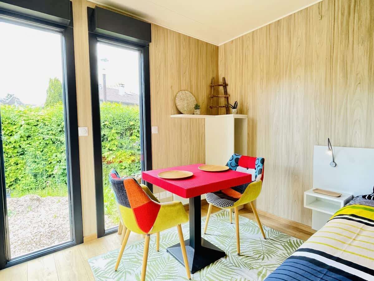 Une chambre moderne dotée d’une grande fenêtre, d’une table à manger avec des chaises, d’un lit et d’une petite table de chevet.