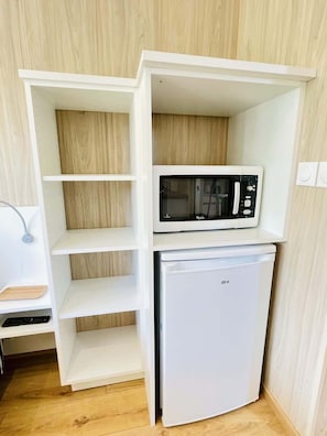 A compact kitchen with a microwave and a refrigerator, wooden shelves, and a small countertop. - Cabane de Rafaël (Vittel)