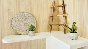A white shelf with two potted plants and a woven wall hanging against a wooden wall. - Cabane de Rafaël (Vittel)