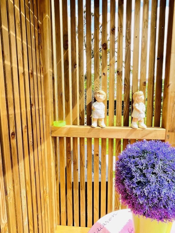 A wooden fence with two small figurines on a shelf, and a potted plant with purple flowers.