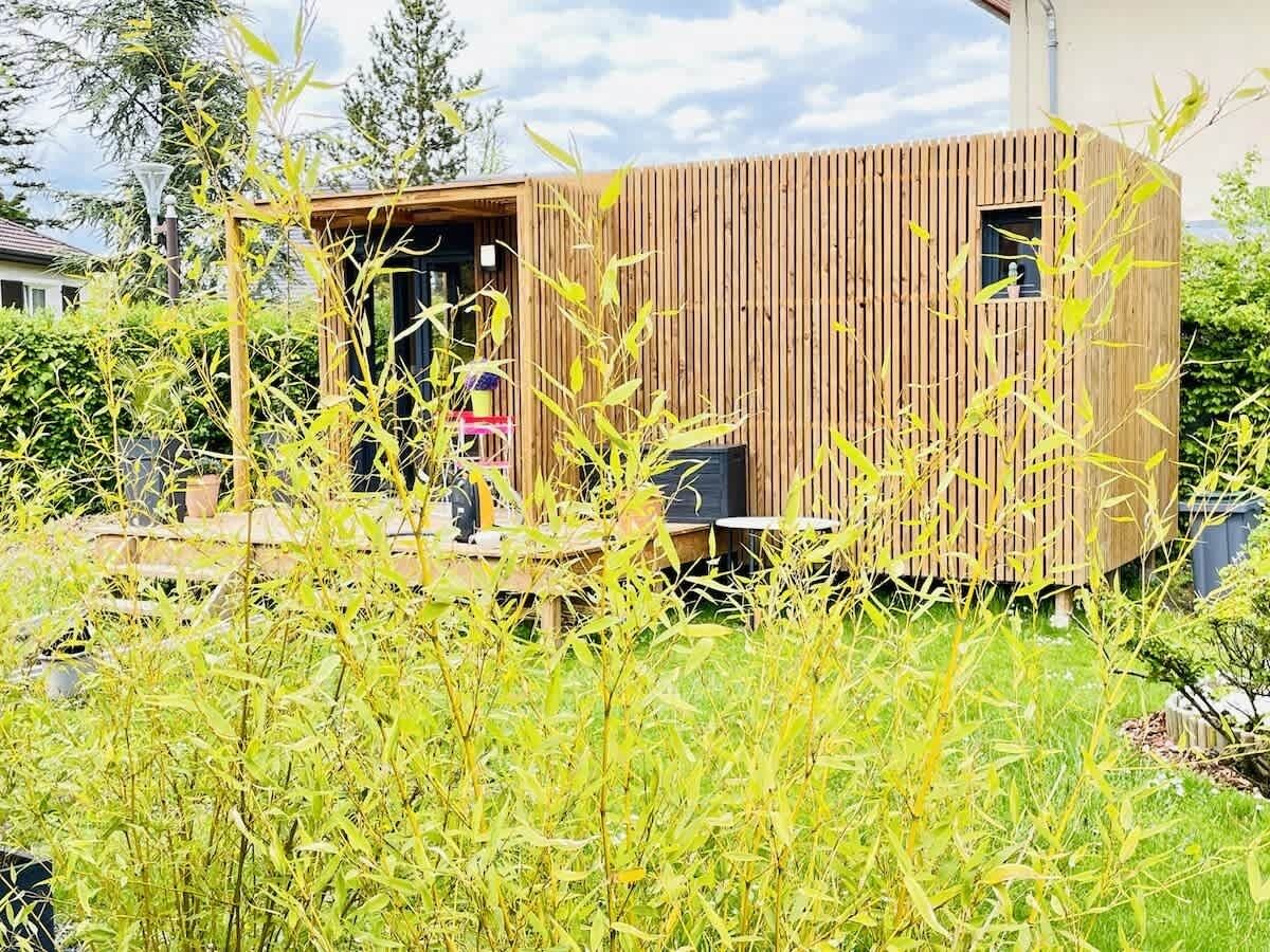 Een klein houten gebouw met een deur en ramen, omringd door groen.
