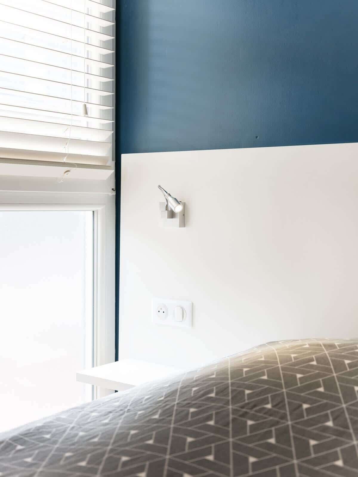 A bedroom with a bed, a wall-mounted light fixture, and a power outlet.
