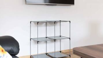 A modern living room with a mounted TV, a metal shelving unit, a wooden dining table, and a black leather sofa.