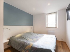 Un dormitorio con cama, ventana, mesita de noche y luz fijada en la pared.