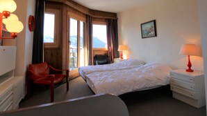 A hotel room with a bed, a chair, a desk, and a window with a view of mountains.