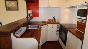A compact kitchen with white cabinets, a wooden countertop, a built-in dishwasher, a kettle, and a stove.