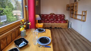 A cozy room with a wooden table set for two, a red sofa, and a window with a view of trees and mountains. - Cozy studio in Avoriaz for 2 pers with Wifi (Avoriaz)