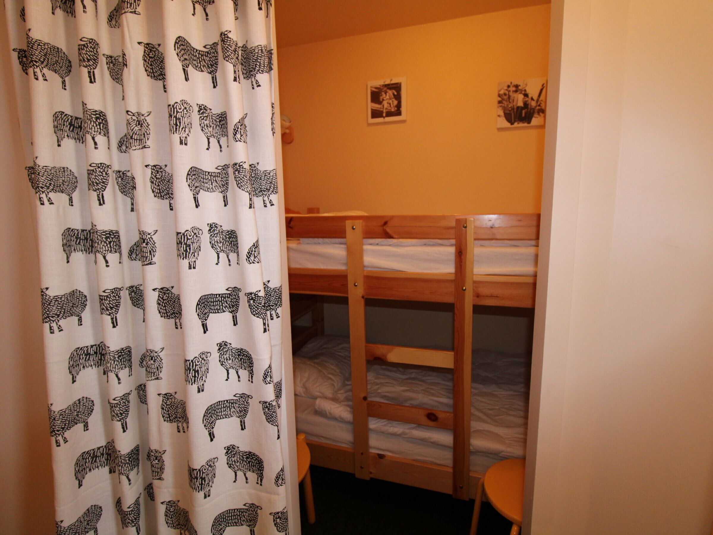 A bedroom with two bunk beds, a curtain with a sheep pattern, and a small table.