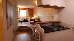Une cuisine compacte dotée d’une cuisinière intégrée, un coin repas avec une table et des chaises, et un espace de vie avec un canapé et une fenêtre.