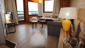 Un salon moderne comprenant un canapé, deux fauteuils, une petite table, une lampe et un téléviseur.