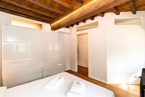 Une chambre avec un plafond en bois, des murs blancs, un lit avec du linge de lit blanc et une armoire intégrée.