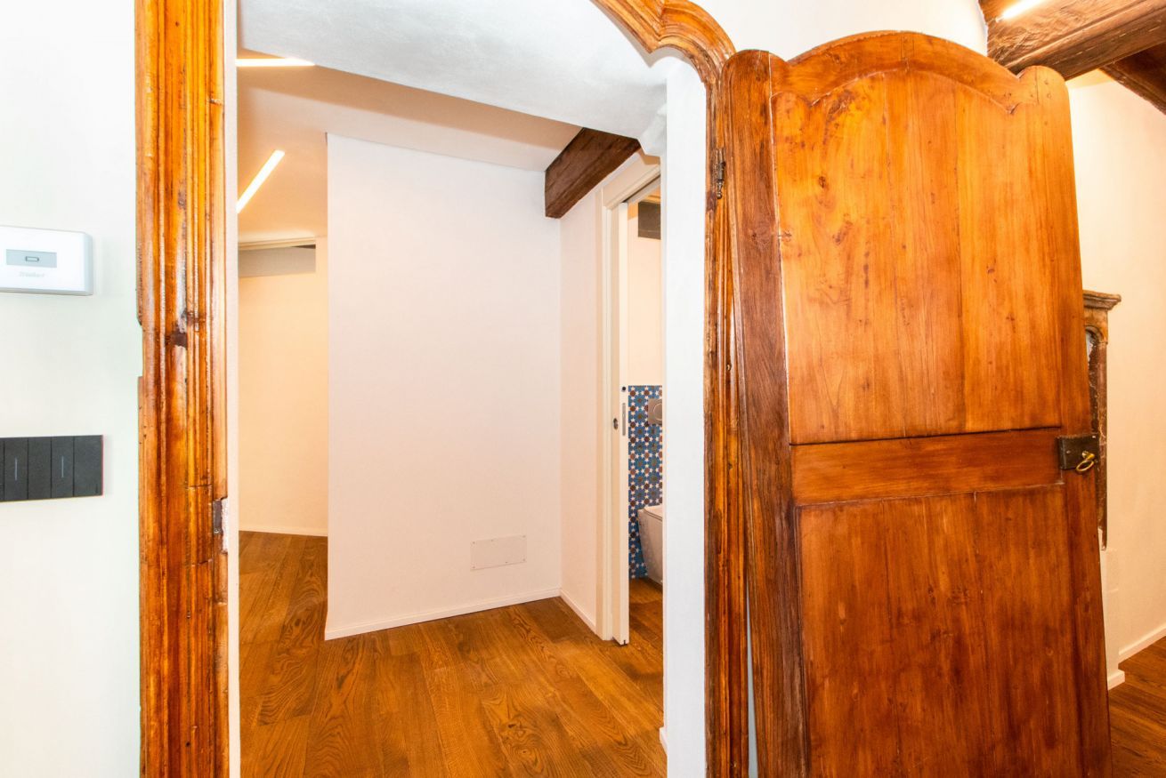 Una puerta de madera que da a un cuarto con pared blanca y suelo de madera.