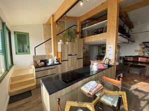 A modern kitchen with a central island, wooden beams, and a staircase leading to an upper level.