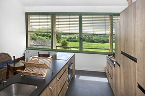 A kitchen with a large window, wooden cabinets, and a black countertop.