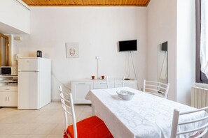 Une pièce comprenant une table à manger, des chaises, un téléviseur, un réfrigérateur et un four à micro-ondes.