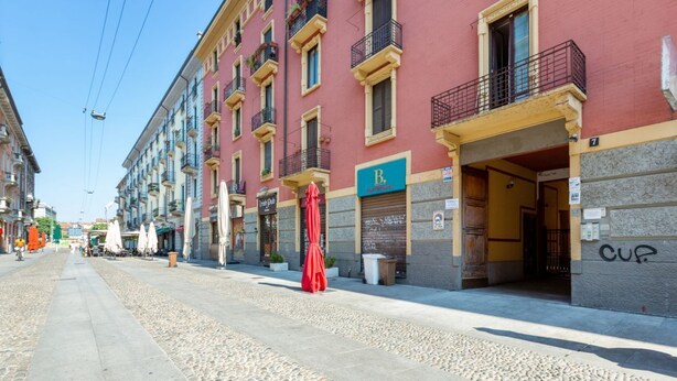Une rue avec un immeuble rouge, une entrée bien visible et une enseigne avec la lettre « R ».