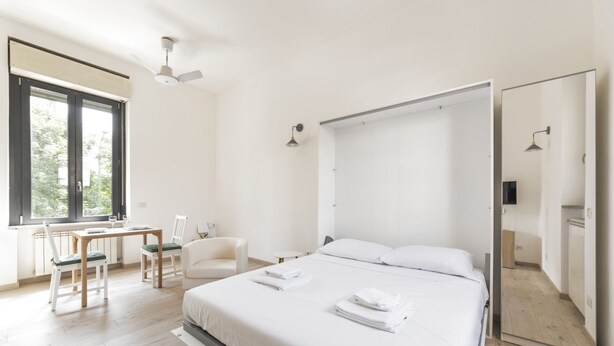 Une chambre d’hôtel moderne avec un grand lit, un bureau avec des chaises, une fenêtre et un miroir.