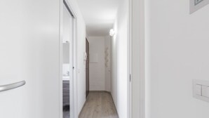 Un couloir étroit avec un plancher en bois, des murs blancs et une porte sur le côté gauche.