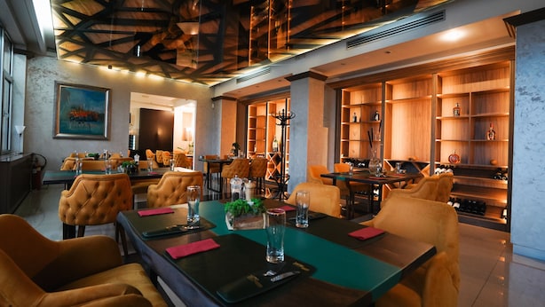 A restaurant with a modern interior, featuring wooden shelves with bottles, a central dining table with chairs, and a ceiling with exposed beams. - Hotel Sumadija (Belgrade)
