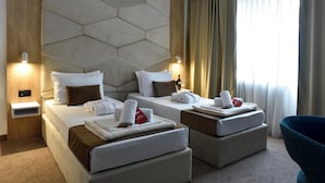 A hotel room with two beds, each with neatly folded towels and pillows, a wooden headboard, and a large window with curtains. - Hotel Sumadija (Belgrade)