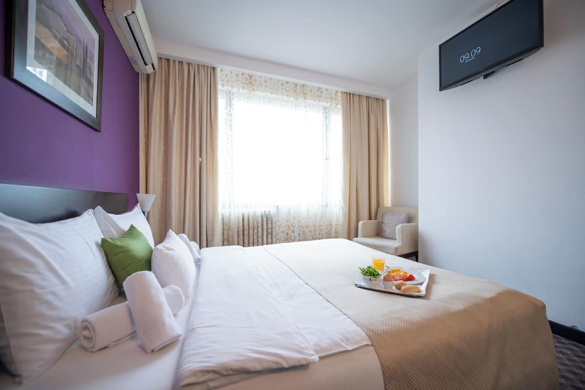 Quarto de hotel com cama, televisão, janela com cortinas e bandeja de café da manhã sobre a cama.