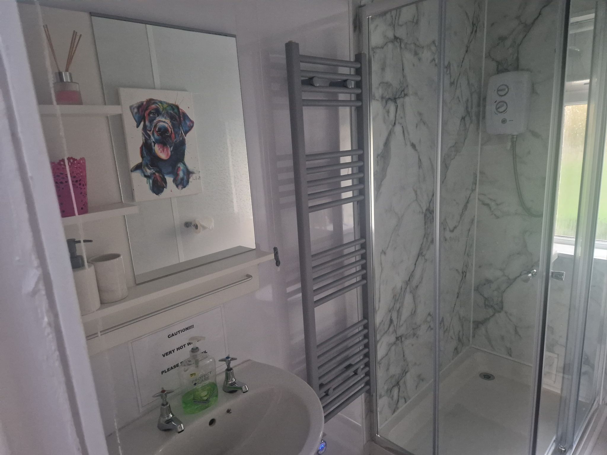 A bathroom with a marble shower, a sink with a soap dispenser, and a towel rack.