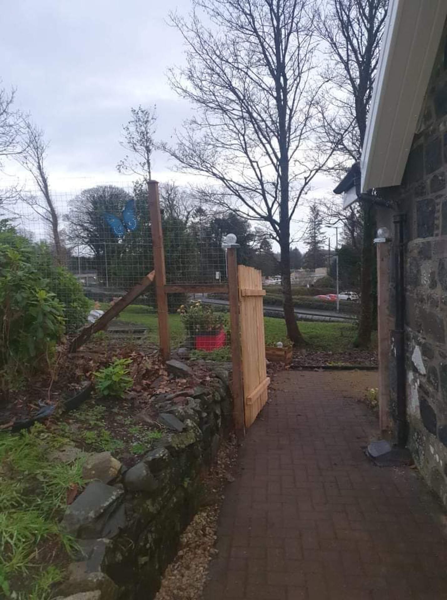 A pathway leading to a wooden gate, surrounded by a stone wall and greenery.