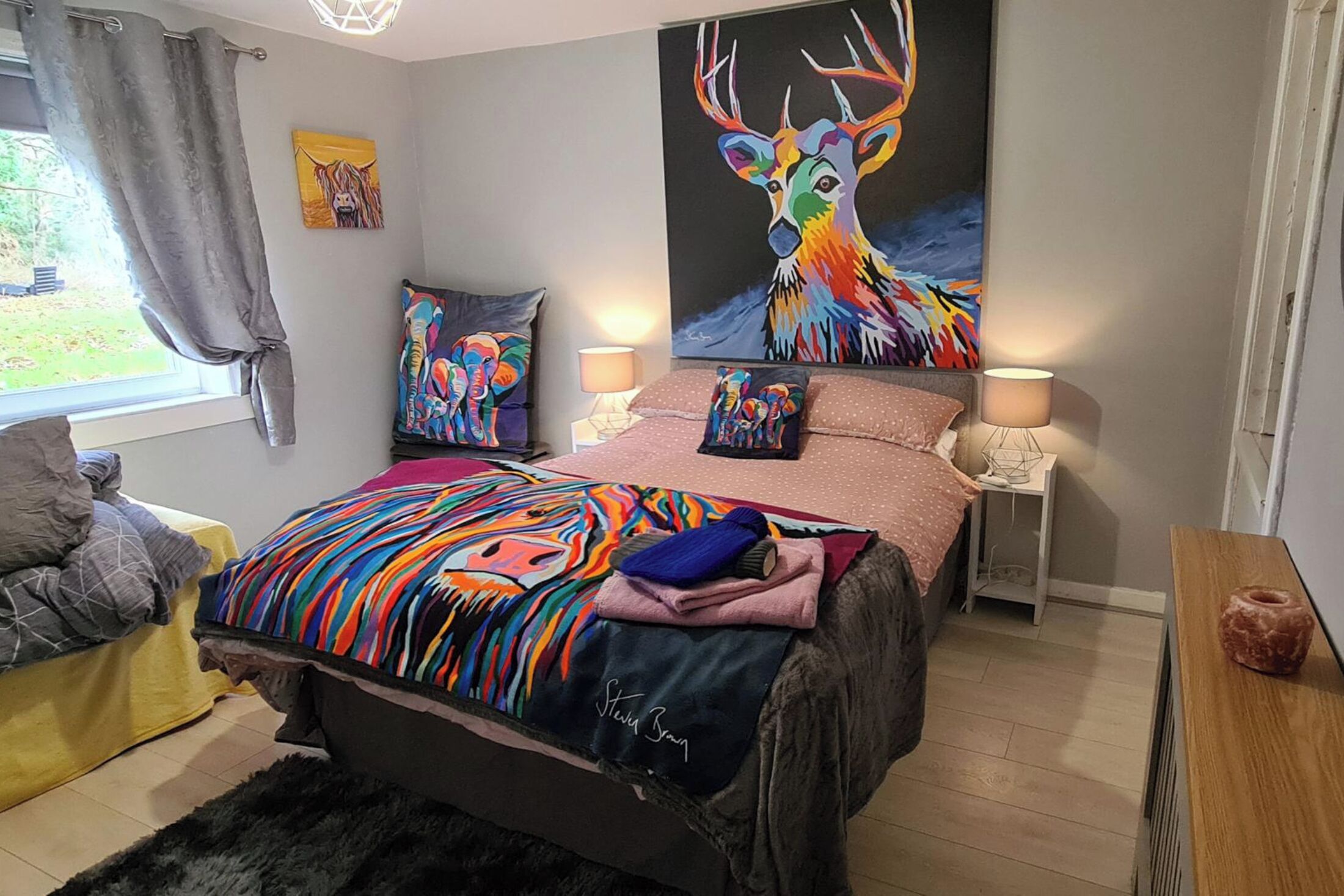 Una camera da letto con un letto grande, due comodini, una finestra con tende e un quadro che raffigura un cervo.