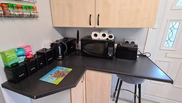A kitchen with a microwave, toaster, and coffee maker. There are spice jars on the wall and a painting on the counter.