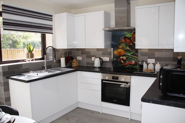 A modern kitchen with white cabinets, a black countertop, a Bosch oven, and a window with a plant.