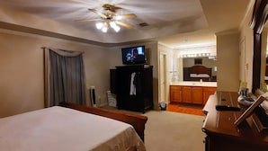 Een hotelkamer met een bed, een plafondventilator, een televisie en een kitchenette.