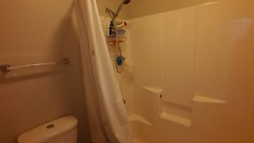 A bathroom with a toilet, a shower with a curtain, and a shelf with toiletries.