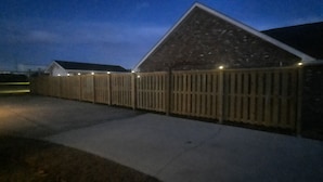 Een woonhuis met een bakstenen gevel, een houten omheining en een oprit van beton.