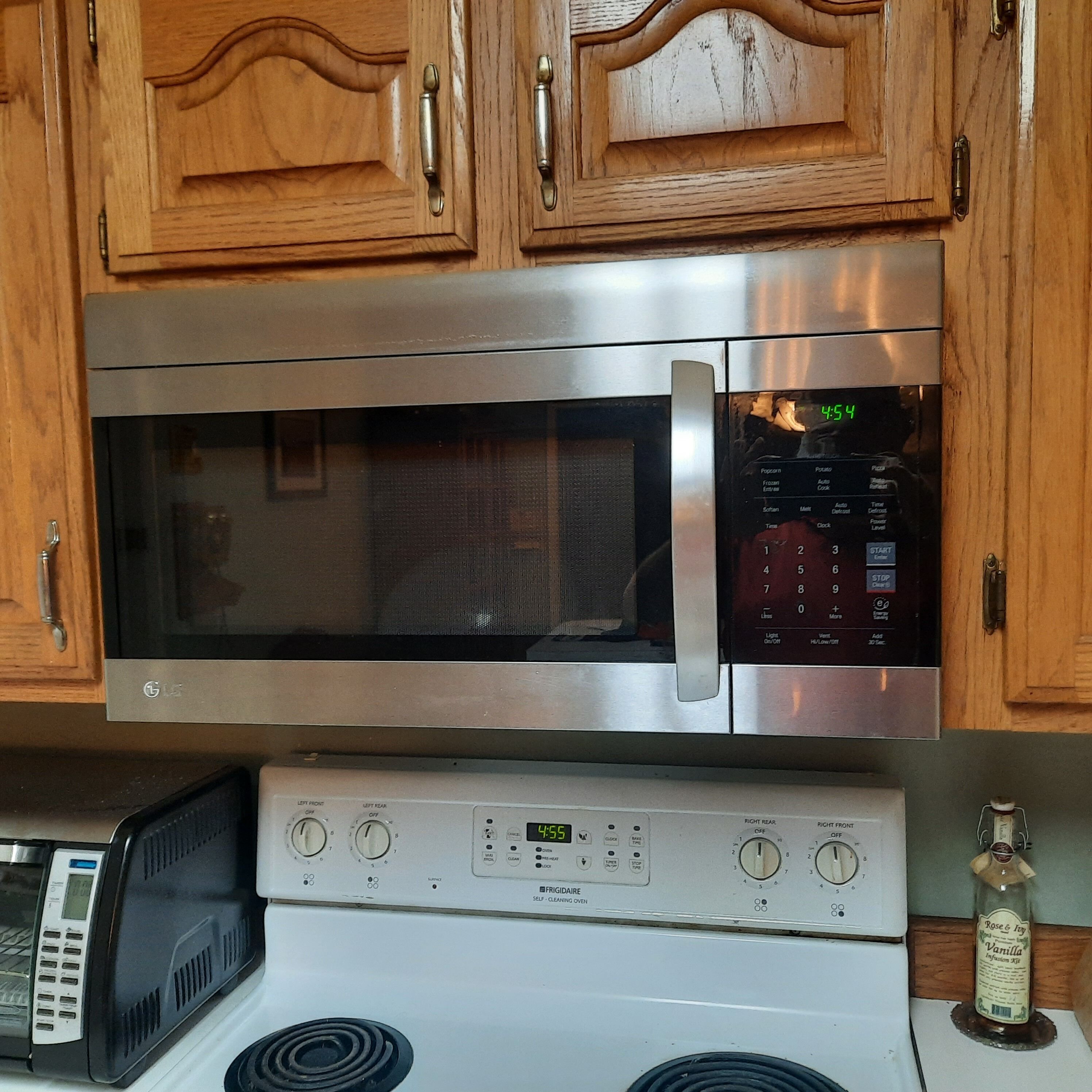 Una cocina con microondas de acero inoxidable, horno autolimpiante y un reloj digital que marca las 4:54.
