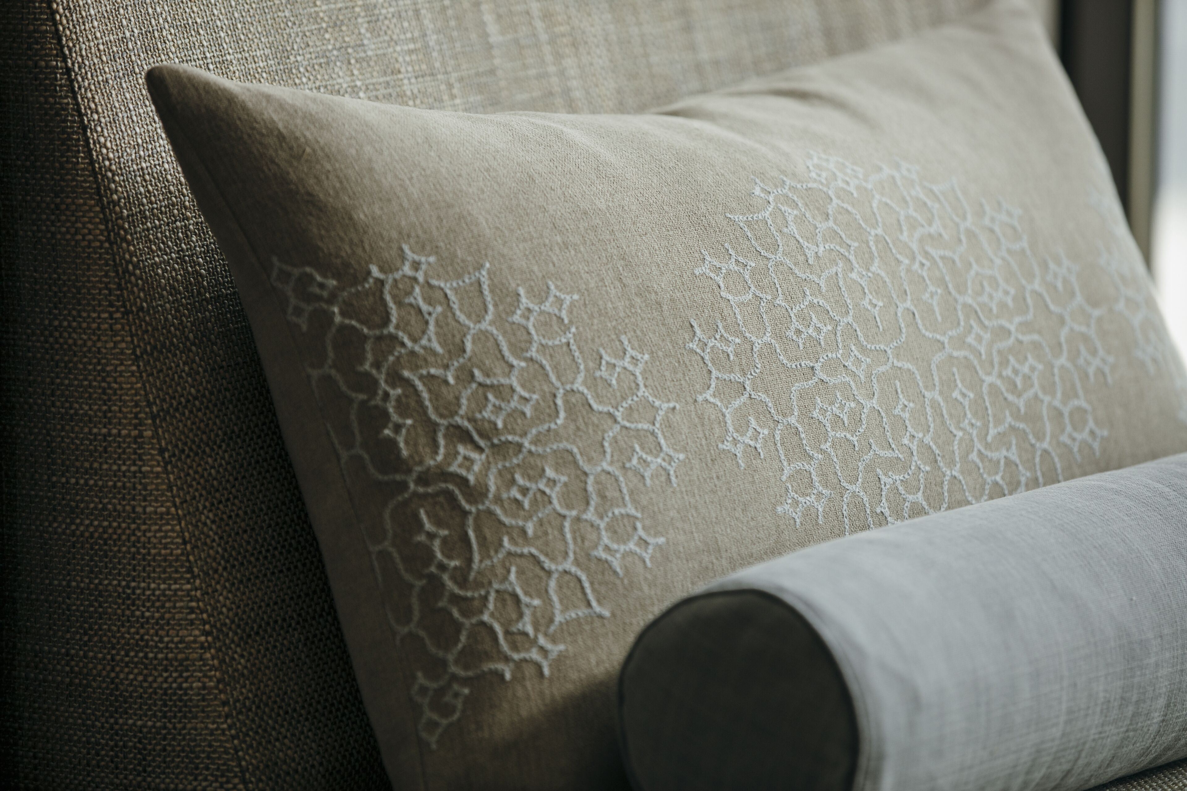A close-up of a beige pillow with a lace pattern on a textured fabric.