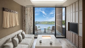 Ein modernes Wohnzimmer mit großem Fenster, einer Couch, einem Couchtisch und einem Fernseher.