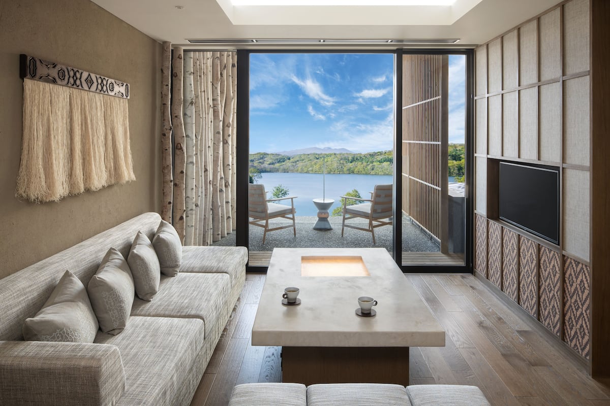 Ein modernes Wohnzimmer mit großem Fenster, einer Couch, einem Couchtisch und einem Fernseher.