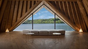Ein Dachzimmer mit Holzbalkendecke, einem großen Fenster, einer Couch und zwei kleinen Tischen.