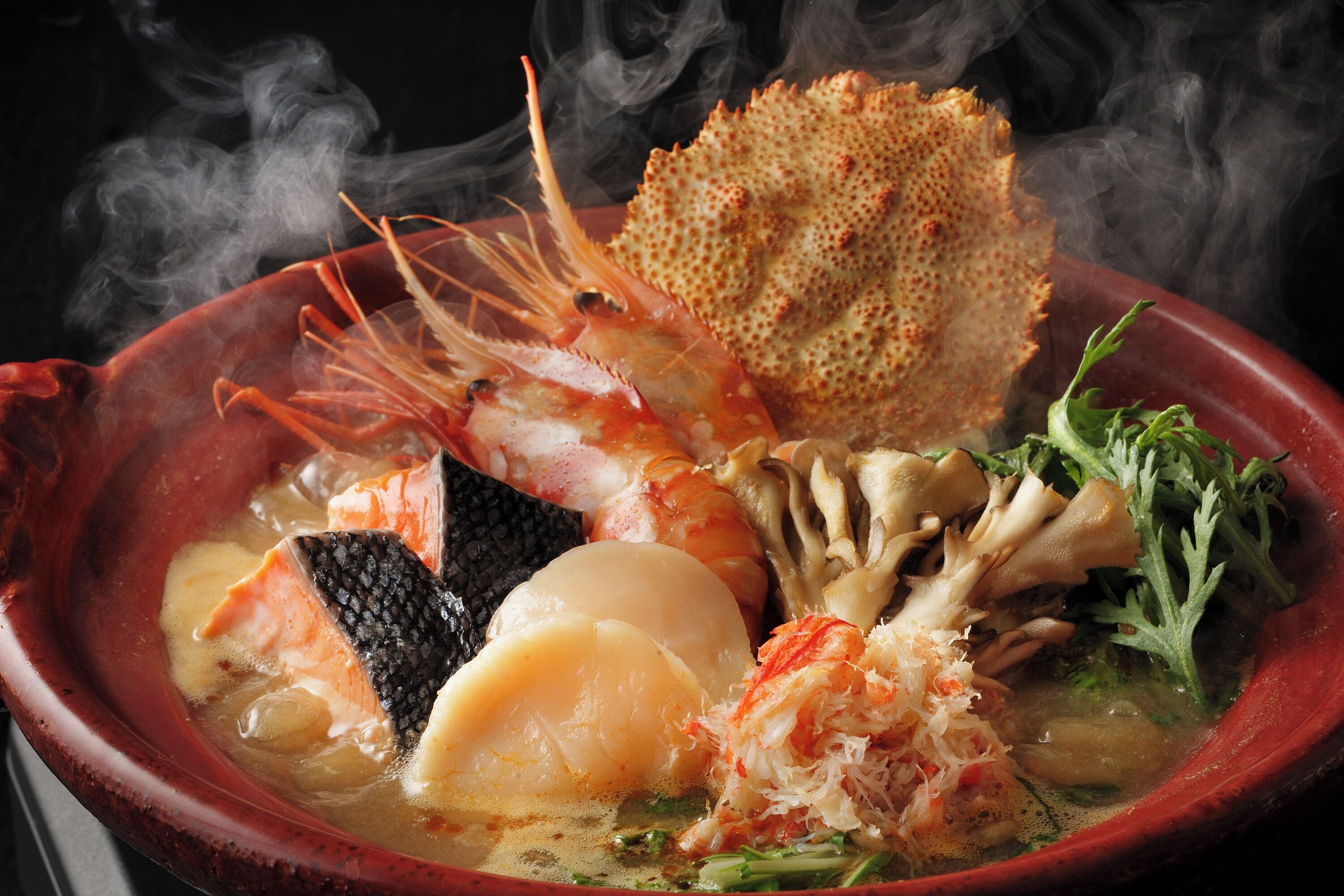 A bowl of seafood soup with various ingredients like shrimp, scallops, and seaweed.