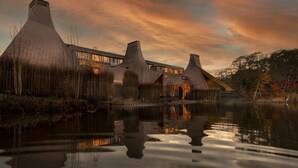 Ein modernes Gebäude mit einem einzigartigen architektonischen Design, das mehrere konische Dächer und ein reflektierendes Wasserelement im Vordergrund zeigt.