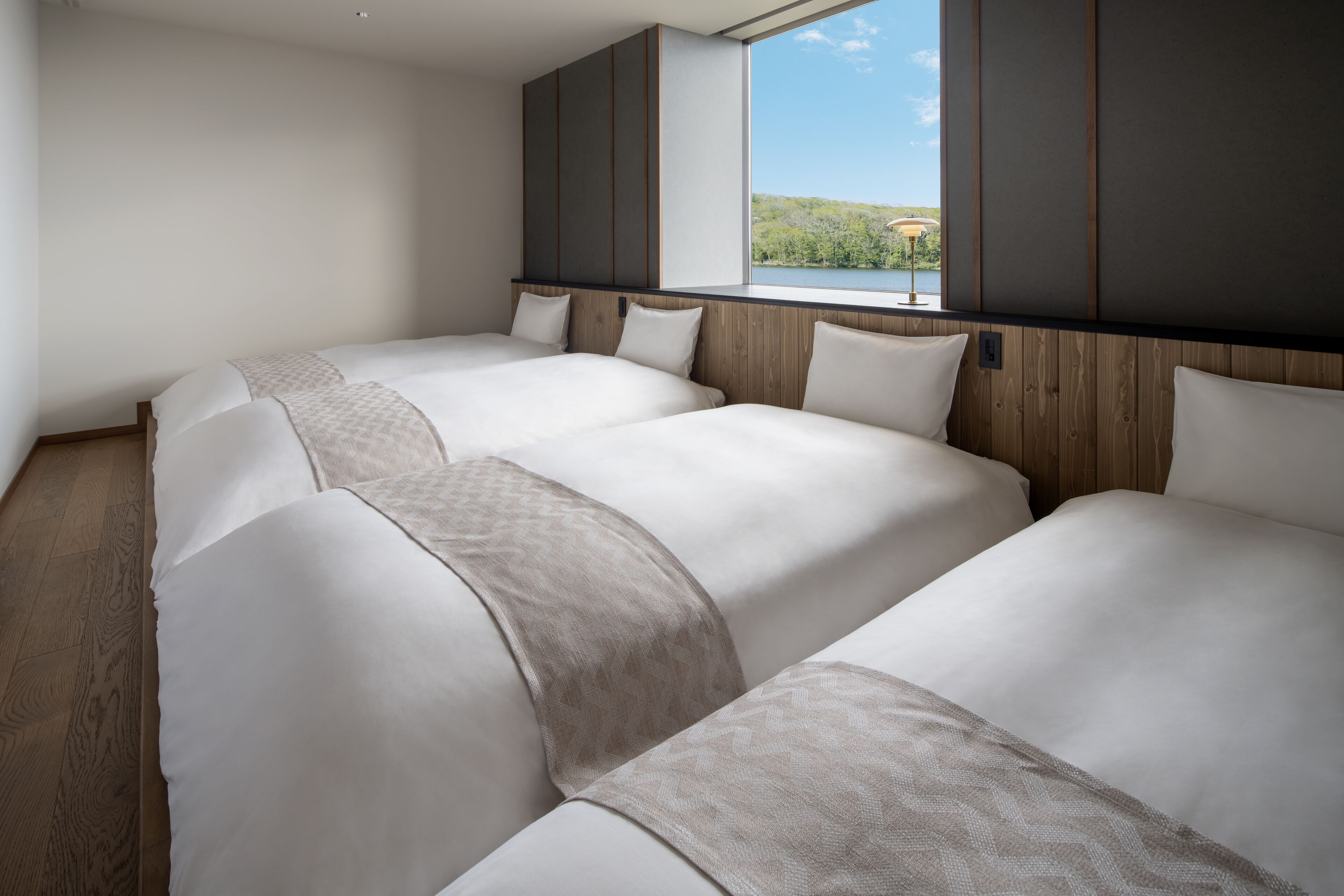 A hotel room with a large window, wooden paneling, and three beds.