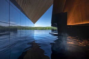Ein modernes Gebäude mit Glasfassade, das eine Landschaft und einen Poolbereich mit Holzboden reflektiert.