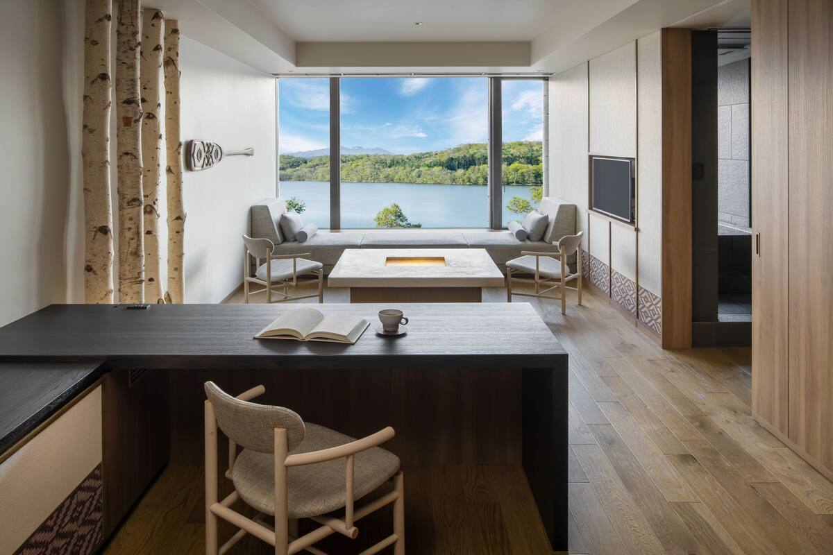 Ein modernes Zimmer mit großem Fenster und Seeblick, einer Essecke mit Tisch und Stühlen sowie einer Küchenzeile mit Arbeitsfläche und Sitzgelegenheiten.