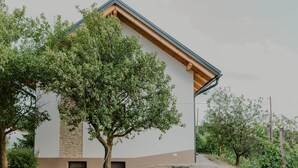 A modern building with a stone base and a white upper section, surrounded by trees and a gravel path. - Haloze hills in your hand (Cirkulane)