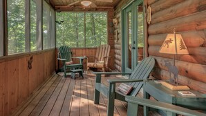 A wooden cabin with a porch featuring Adirondack chairs, a table, and a lamp. - Log Cabin, Rumbling Bald Resort Amenities - Autumn Ridge by Carolina Properties (Lake Lure)