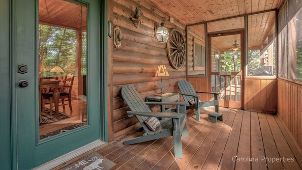 A wooden cabin with a porch, Adirondack chairs, a small table, and a large wooden wheel. - Log Cabin, Rumbling Bald Resort Amenities - Autumn Ridge by Carolina Properties (Lake Lure)