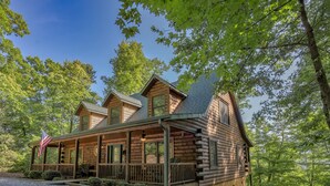 A log cabin with a porch, multiple windows, and a flag. - Log Cabin, Rumbling Bald Resort Amenities - Autumn Ridge by Carolina Properties (Lake Lure)