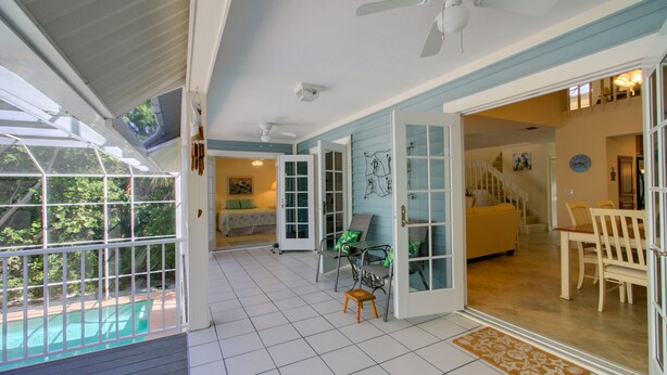 A spacious indoor area with a pool view, open doors leading to another room, and a ceiling fan.