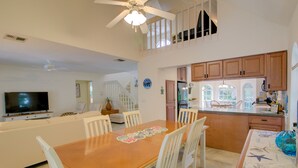 A spacious kitchen with wooden cabinets, a dining area with a wooden table and white chairs, and a TV in the living area.