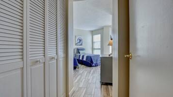 A hallway leading to a bedroom with a bed, a nightstand, and a window.